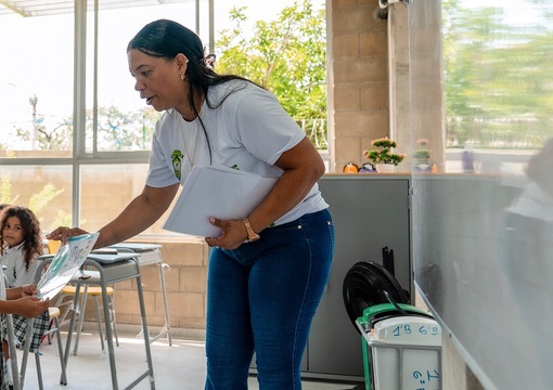 Docente en salón de clase junto a sus estudiantes.