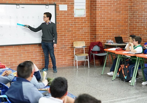 Docente en salón de clase junto a sus estudiantes.