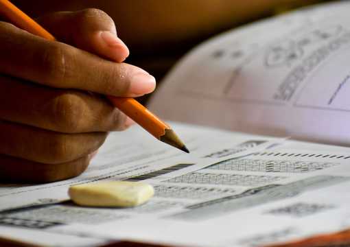 Imagen de una mano con un lápiz y un borrador sobre un cuadernillo de preguntas