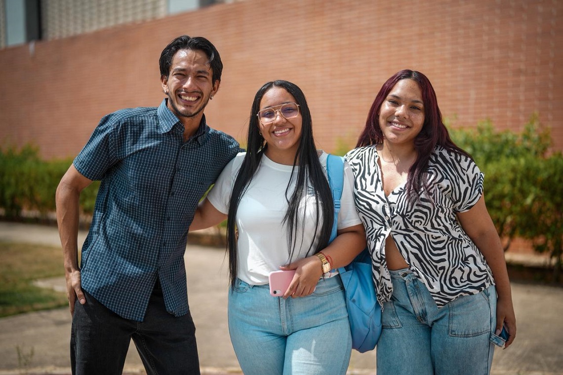 Tres jóvenes estudiantes, dos mujeres y un hombre sonriendo a la cámara