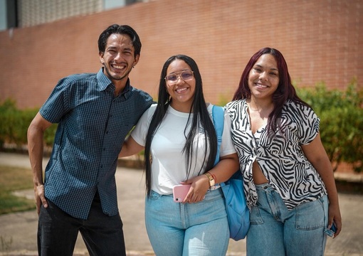 Tres jóvenes estudiantes, dos mujeres y un hombre sonriendo a la cámara