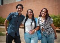 Tres jóvenes estudiantes, dos mujeres y un hombre sonriendo a la cámara