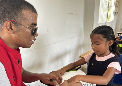 Profesor tiflologo guía a estudiante con discapacidad visual en la lectura del braille